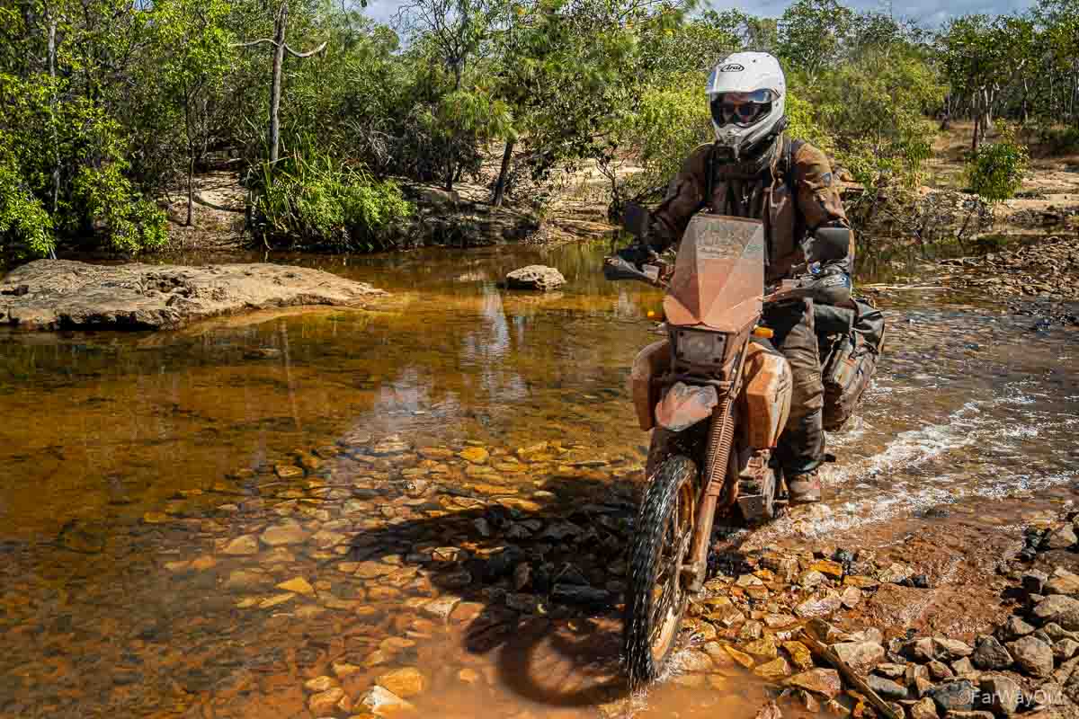 motorcycle rider on dr650 crossing a river in cape york